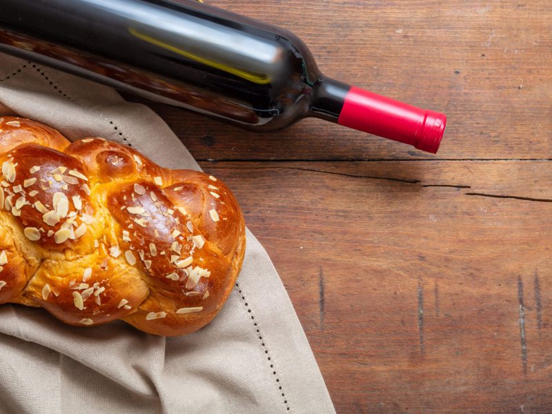 Shabbat concept, challah bread with a bottle of red wine on wooden table, copy space, top view