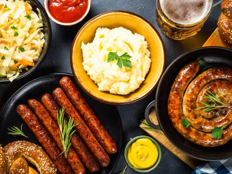 Oktoberfest food. Holiday german dishes - sauerkraut, sausage, pretzel, mashed potato and beer. Top view on black table.